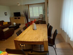 A dining area with a wooden table and chairs, a sofa, a TV, and a window with curtains. - Auf der Matta E01 Appartement/Fewo, Dusche oder Bad, WC 4½-Zimmerwohnung by Interhome (Davos)