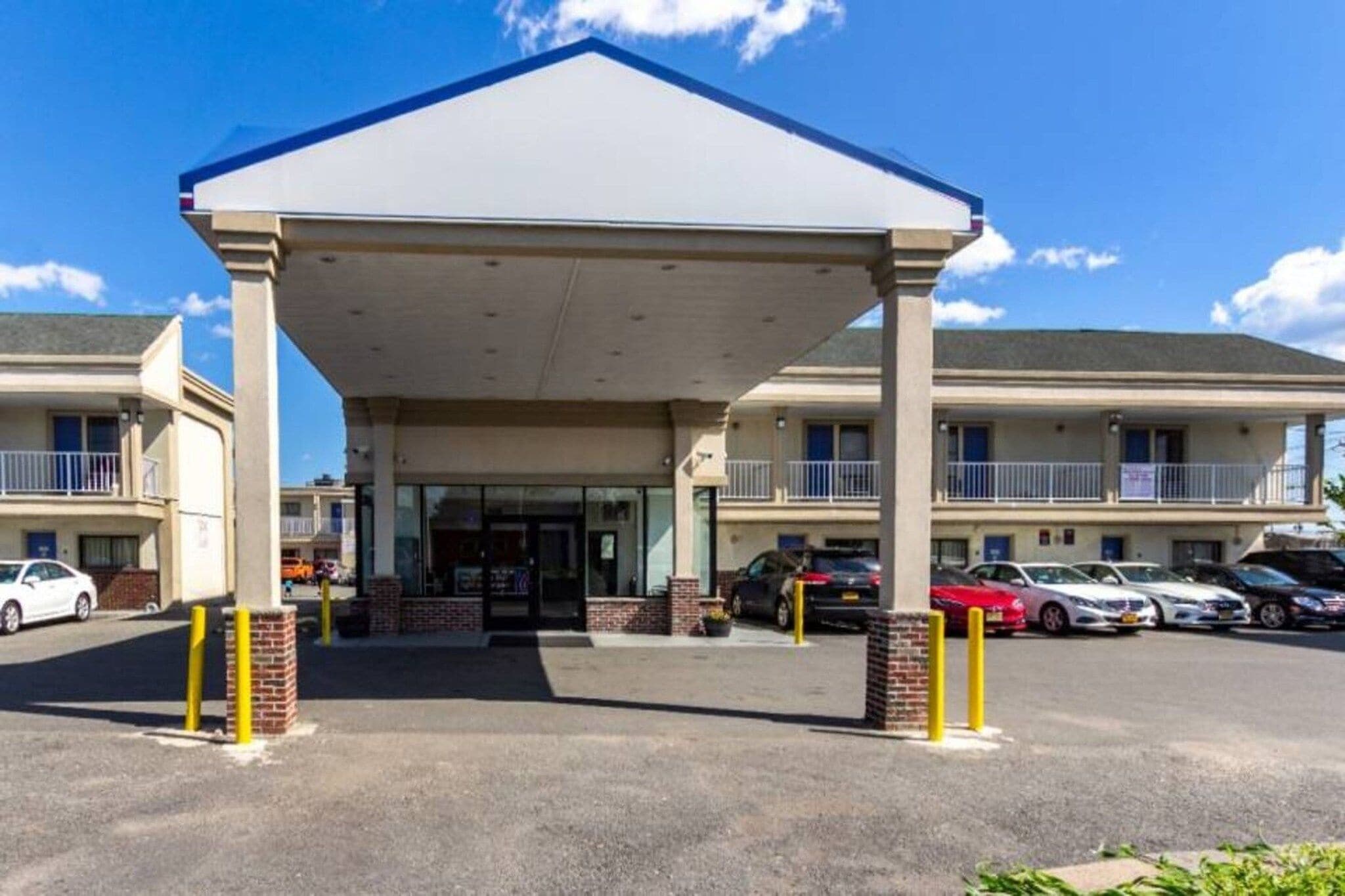 Un hotel con entrada cubierta, varios balcones y un estacionamiento con coches.