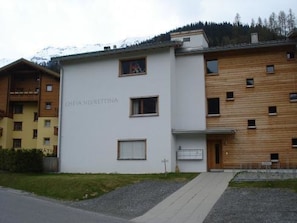 A modern building with a sign reading 'CHESA HUIRETTINA.' It features a flat facade with multiple windows and a wooden section on the right. - Chesa Silvrettina D4 Appartement/Fewo, Dusche oder Bad, WC 4½-Zimmerwohnung by Interhome (Klosters)