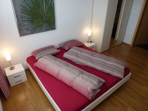 A bed with red bedding, two bedside tables with lamps, and a wall-mounted artwork. - Chesa Silvrettina D4 Appartement/Fewo, Dusche oder Bad, WC 4½-Zimmerwohnung by Interhome (Klosters)