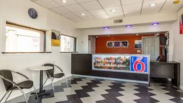 A hotel lobby with a check-in counter, a seating area with two chairs, and a patterned floor.