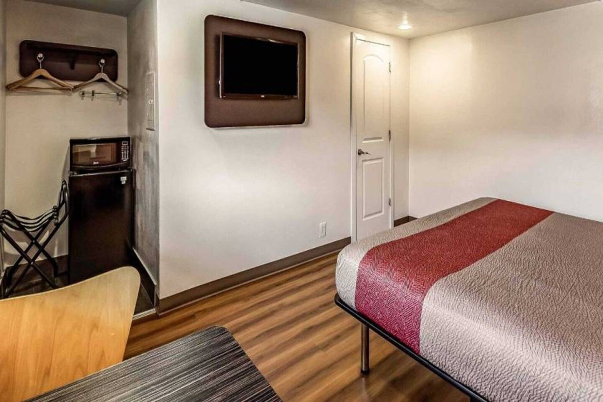Una habitación de hotel con una cama, un escritorio con silla, un televisor y un armario.