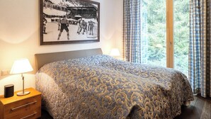 Ein Hotelzimmer mit einem Bett, einem Nachttisch, einer Lampe, einem Fenster mit Vorhängen und einem gerahmten Bild an der Wand.