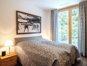 A hotel room with a bed, a nightstand, a lamp, a window with curtains, and a framed picture on the wall. - Scarlett Suot 63 Appartement/Fewo, Dusche oder Bad, WC 4-Zimmerwohnung by Interhome (Davos)