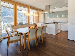 Eine moderne Küche mit einer zentralen Kochinsel, einem Holzespeisetisch mit Stühlen und großen Fenstern mit Blick auf die Berge.