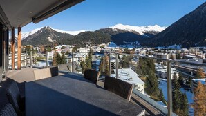Ein Balkon mit Blick auf ein verschneites Gebirge und eine darunterliegende Stadt.