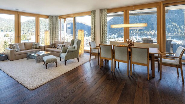 Ein geräumiges Wohnzimmer mit großem Fenster, einer Sofagarnitur, einem Couchtisch und einem Essbereich mit Stühlen und Tisch.