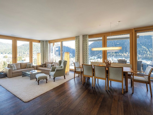 A spacious living room with a large window, a sofa set, a coffee table, and a dining area with chairs and a table. - Scarlett Suot 63 Appartement/Fewo, Dusche oder Bad, WC 4-Zimmerwohnung by Interhome (Davos)