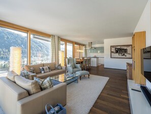 Ein modernes Wohnzimmer mit Sofa, Couchtisch und Blick auf eine Berglandschaft durch große Fenster.