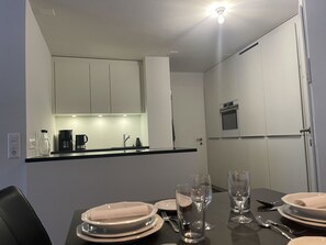 A modern kitchen with white cabinets, a black countertop, and a dining area set for four with plates, glasses, and cutlery. - Rex 33 Appartement/Fewo, Dusche oder Bad, WC 2½-Zimmerwohnung by Interhome (Davos)