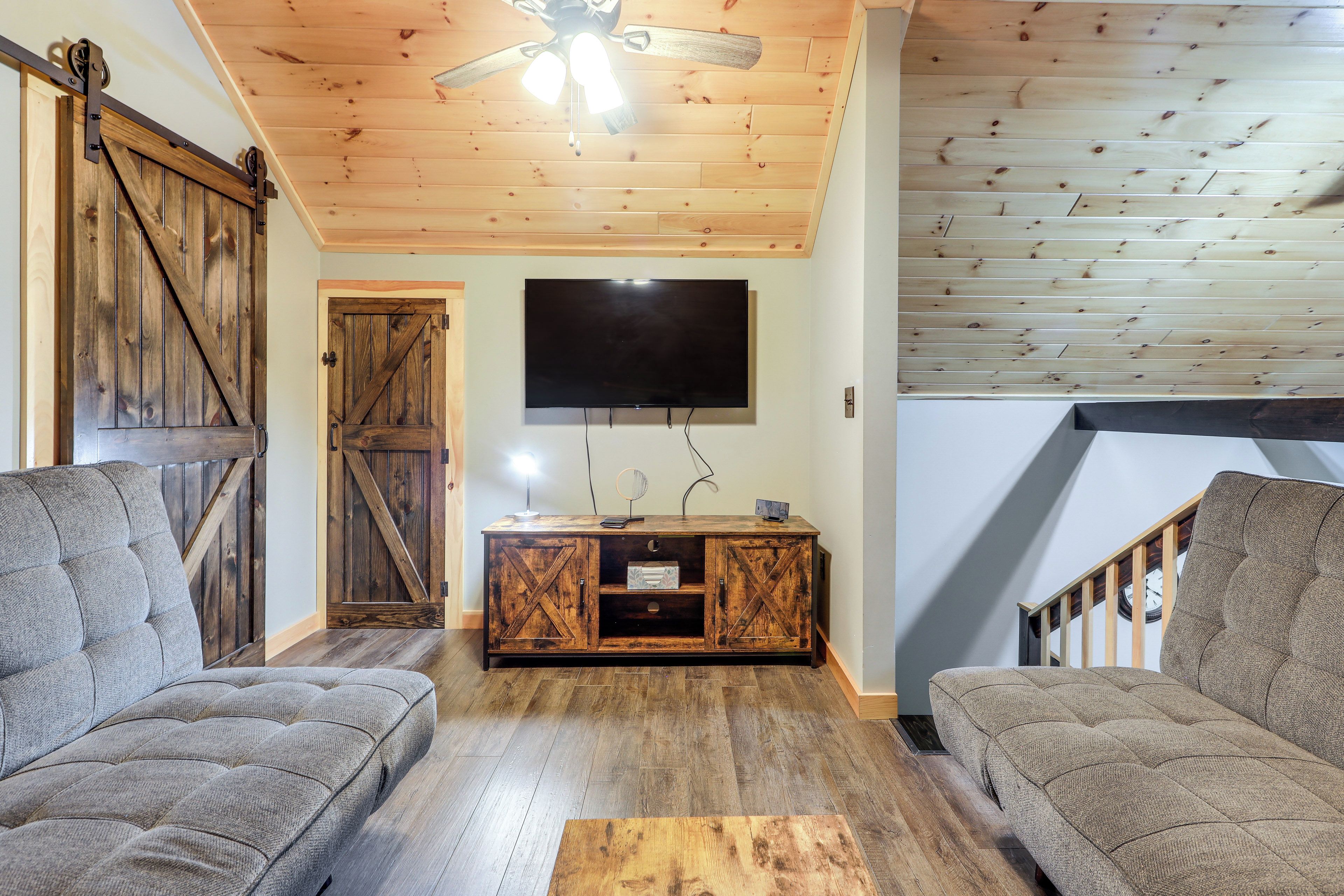 Una sala de estar acogedora con techo de madera, un televisor grande montado en la pared y un mueble de madera rústico.