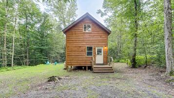 A small wooden cabin with a front porch and a door, surrounded by a forest.
