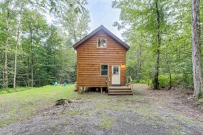 Une petite cabane en bois, dotée d’un porche et d’une porte, entourée d’une forêt.