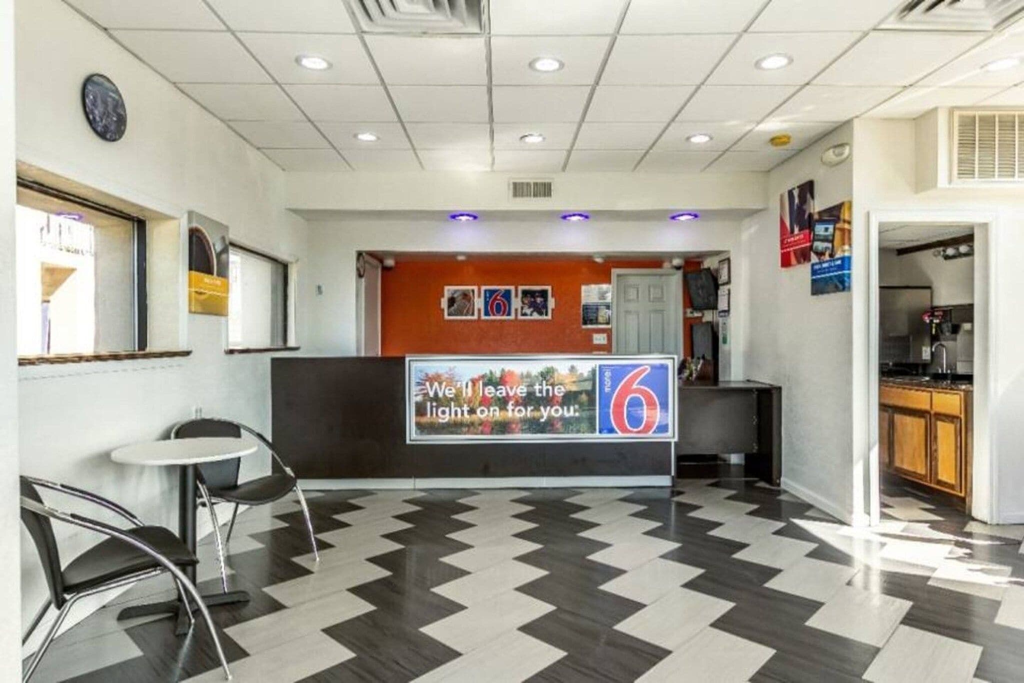 Un vestíbulo de hotel con mostrador de recepción, zona de estar y una cocina visible a través de una puerta abierta.