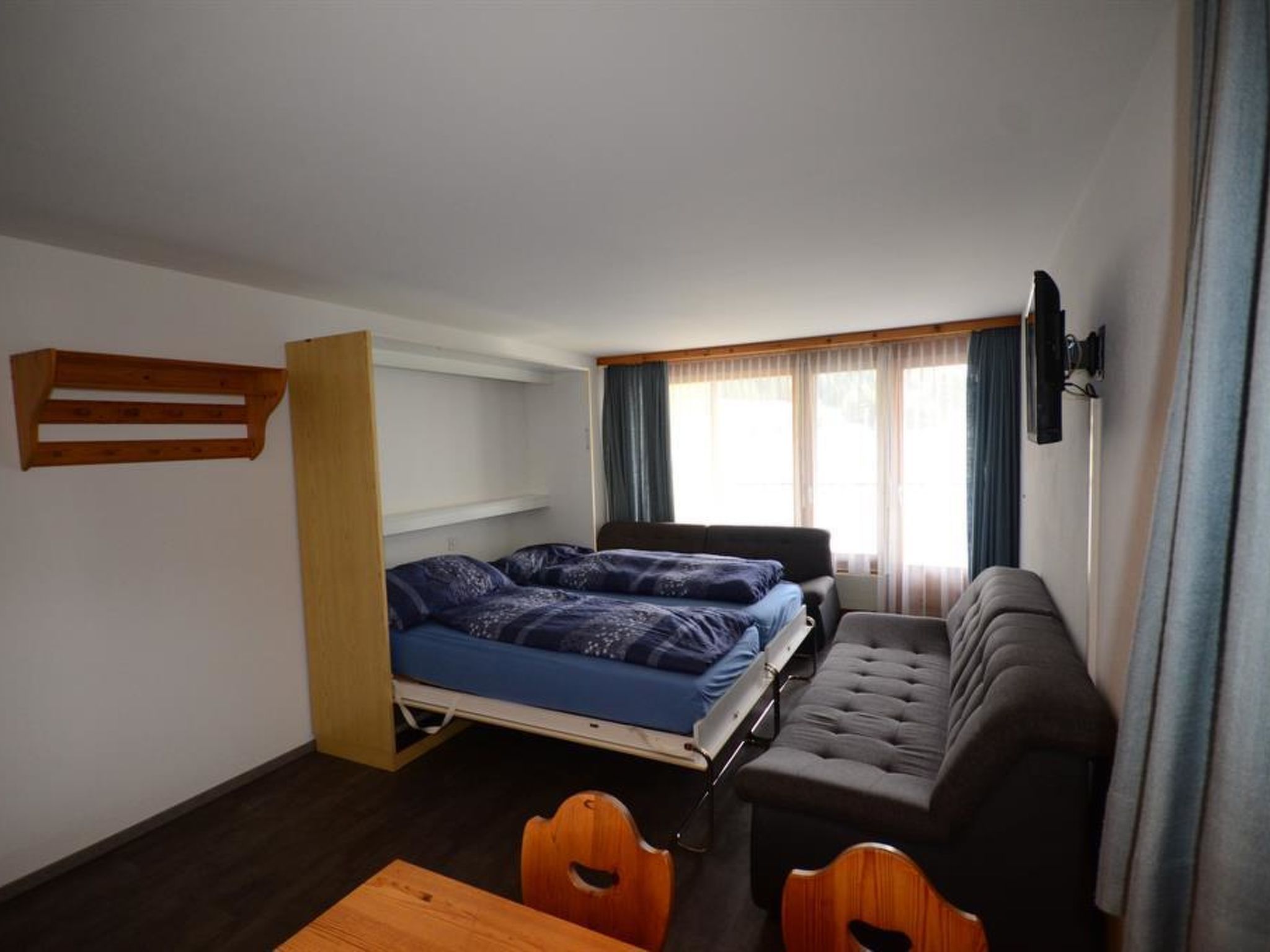 Een kleine kamer met een bed, een slaapbank, een tafel en een televisie.