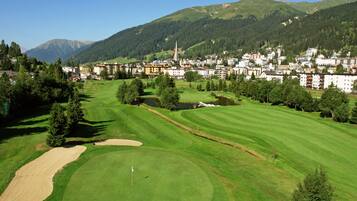 A golf course with a flagstick, surrounded by a residential area with houses and a church.