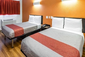 A hotel room with two beds, each with a white and red bedspread, a bedside table with a phone, and a wall-mounted light. - 3 Full Beds | Non-Smoking (ELIZABETH)