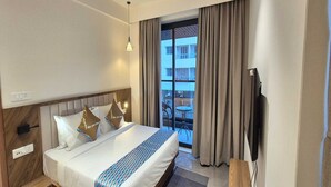 A hotel room with a bed, a TV, a window with curtains, and a balcony with a table and chairs. - Deluxe King Roompalette Fairmont (Gonda)