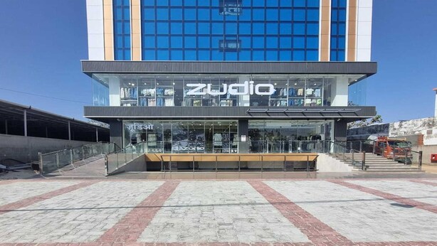 A modern building with a large glass facade, a prominent 'Zudio' sign, and a paved entrance area. - Deluxe King Roompalette Fairmont (Gonda)