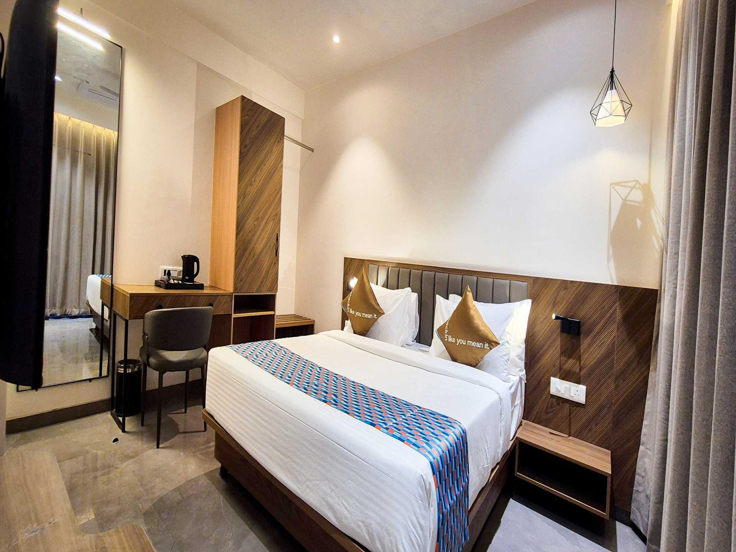 A hotel room with a bed, a desk, a chair, a bedside table, and a hanging light fixture.