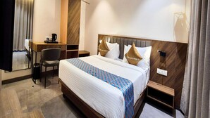 A hotel room with a bed, a desk, a chair, a bedside table, and a hanging light fixture. - Deluxe King Roompalette Fairmont (Gonda)