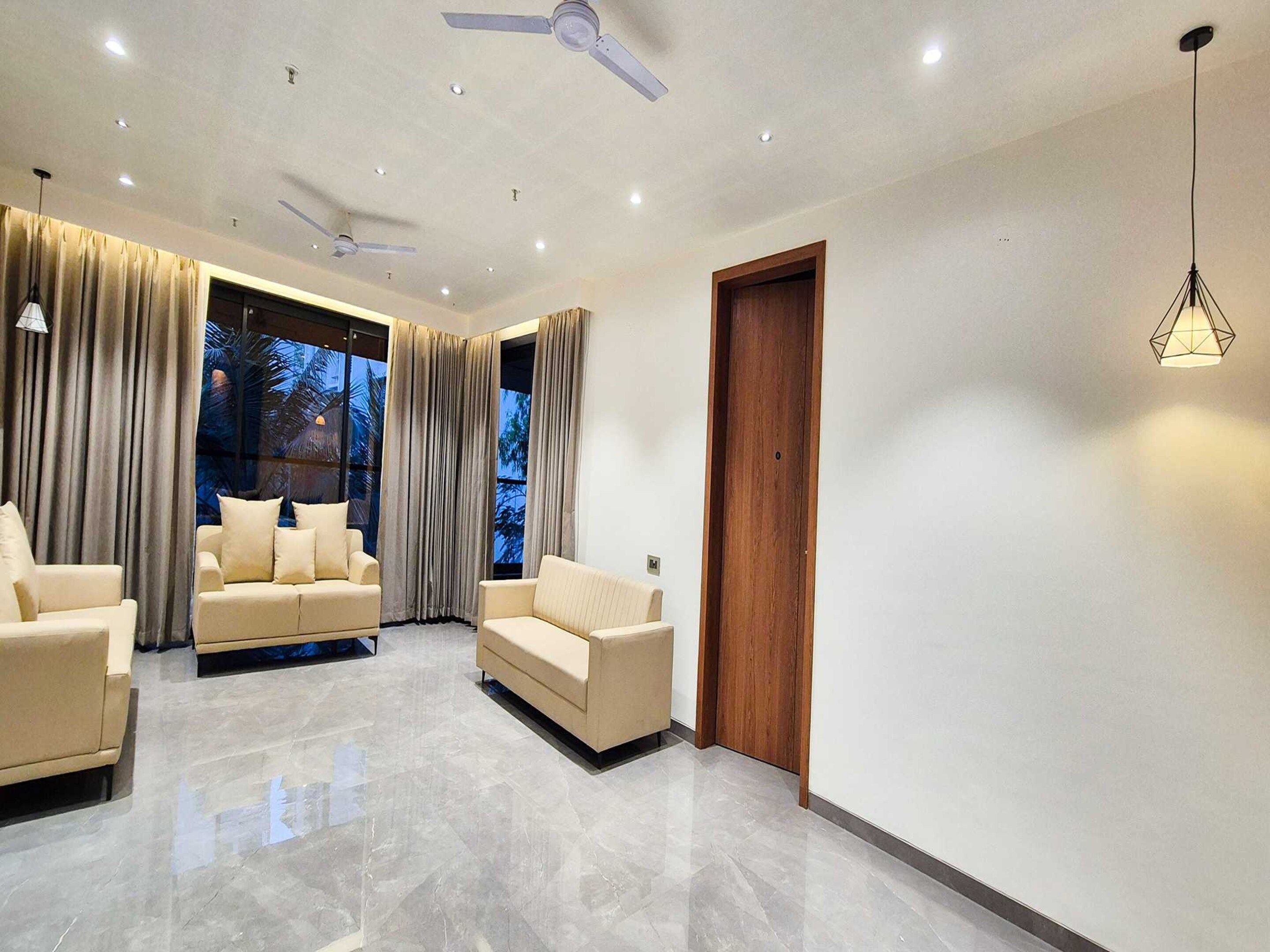 A modern living room with two beige sofas, a ceiling fan, and a wooden door.