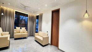 A modern living room with two beige sofas, a ceiling fan, and a wooden door. - Deluxe King Roompalette Fairmont (Gonda)
