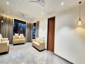 A modern living room with two beige sofas, a ceiling fan, and a wooden door. - Deluxe King Roompalette Fairmont (Gonda)