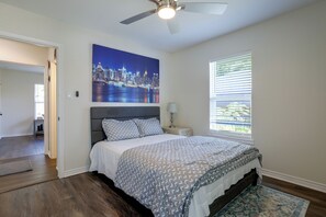 A bedroom with a cityscape painting, a bed with patterned bedding, a ceiling fan, and a window with blinds. - Recently Remodeled Dtwn Frisco Home w/ Yard! (Frisco)