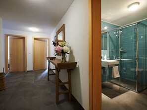 Ein Flur mit einer hölzernen Bank und einem Blumenstrauß, der zu einem Badezimmer mit Duschkabine führt.
