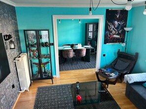 A living room with a glass coffee table, a sofa, a dining area with chairs, and a radiator.