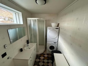 Ein kleines Badezimmer mit Waschbecken, Spiegel, Dusche sowie übereinander angeordneter Wasch- und Trockenmaschine.