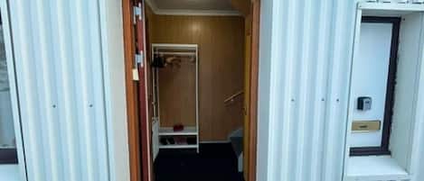 Un vano que da a una habitación con puerta de madera, un pequeño estante y un escalón que conduce a un nivel superior.