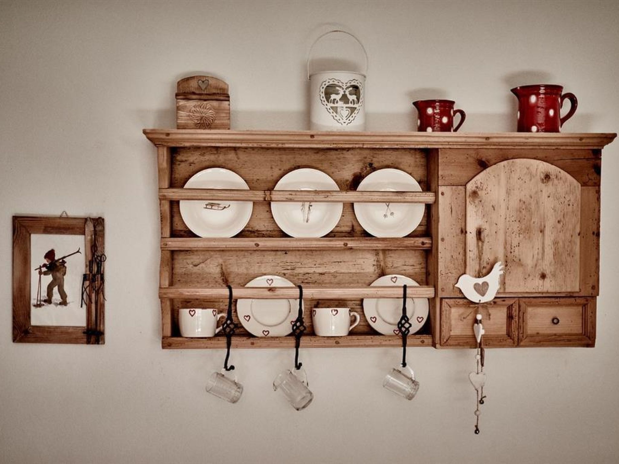 A wooden wall-mounted shelf with plates, cups, and a picture frame.