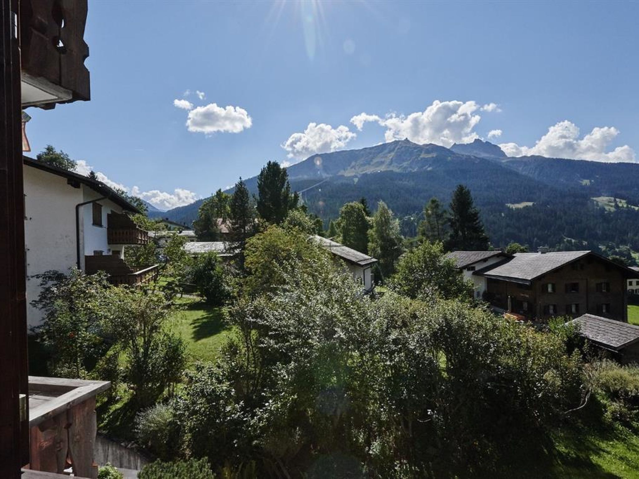 Un paysage de montagne avec un ciel dégagé, des maisons et de la végétation au premier plan.