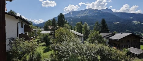 Un paysage de montagne avec un ciel dégagé, des maisons et de la végétation au premier plan.