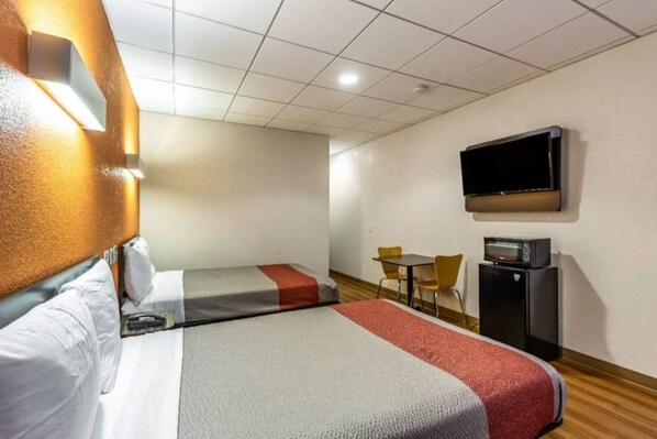 A hotel room with two beds, a television, a desk with a computer, and a chair.
