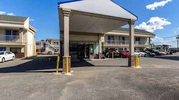 Um motel com entrada coberta, vários espaços de estacionamento e céu aberto.