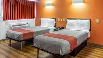Quarto de hotel com duas camas, uma janela com cortinas vermelhas e luminária fixada na parede.