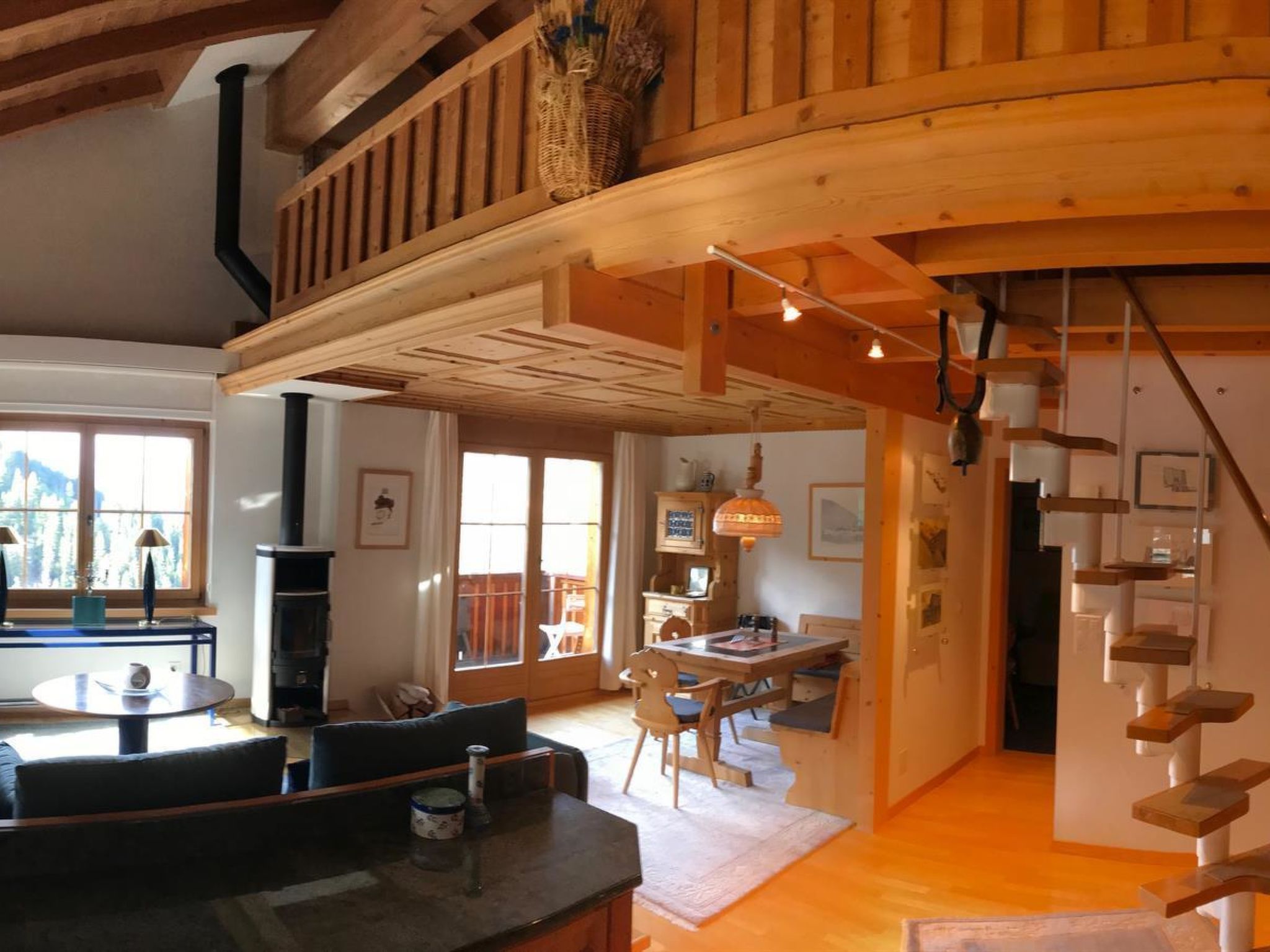 A spacious living area with a high ceiling, wooden beams, a fireplace, a dining area, and a staircase.