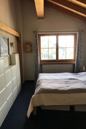 A bedroom with a bed, a dresser, a window with curtains, and a wooden ceiling beam. - Gufer - Maisonett Appartement/Fewo, Dusche oder Bad, WC 3½-Zimmerwohnung by Interhome (Davos)