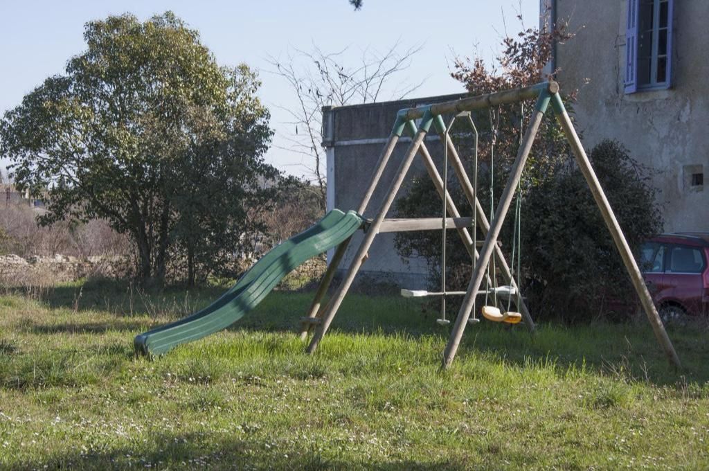 Columpio con tobogán en un área verde con un edificio al fondo.