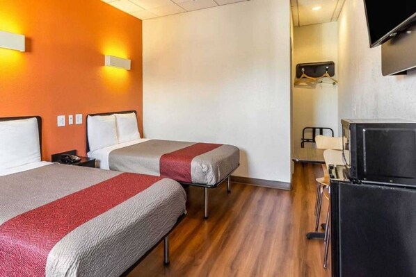 A hotel room with two beds, a television, and a desk with a chair.