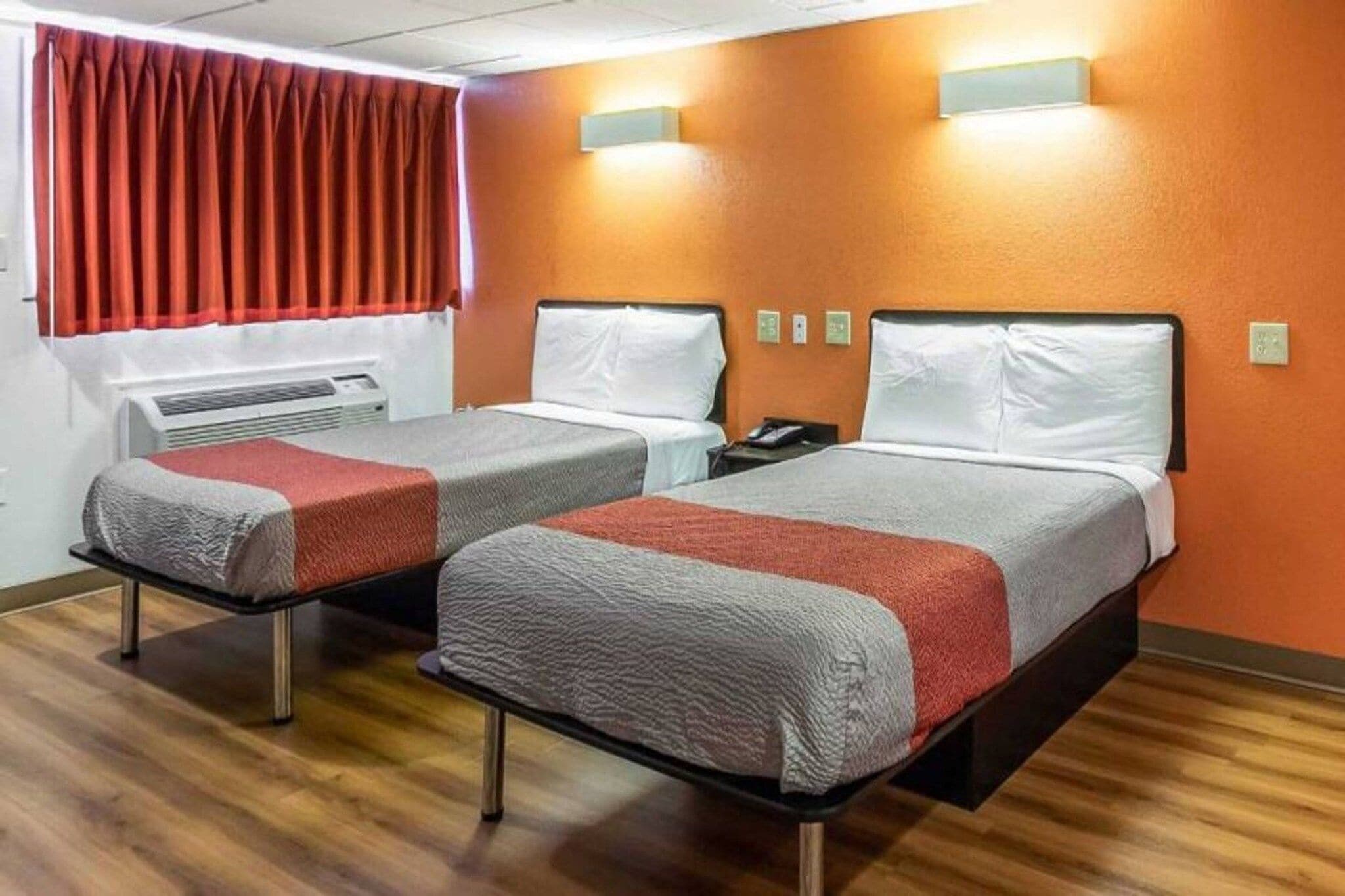 Ein Hotelzimmer mit zwei Betten, einem Fenster mit roten Vorhängen und einer Wandleuchte.