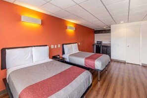 Une chambre d’hôtel avec deux lits, une kitchenette et une porte blanche.
