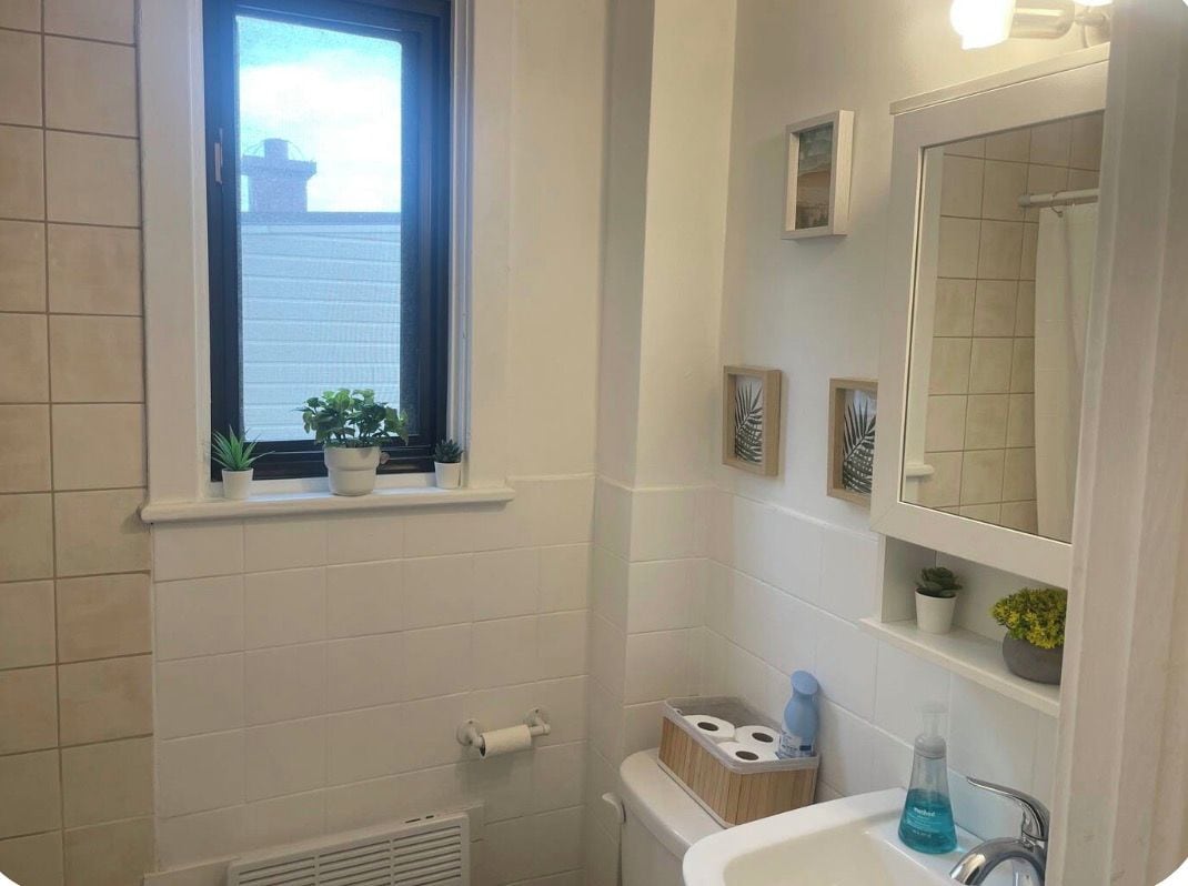 Un bagno con finestra, lavandino, WC e zona doccia.