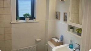 Ein Badezimmer mit Fenster, Waschbecken, Toilette und Duschbereich.