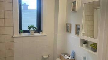 Un bagno con finestra, lavandino, WC e zona doccia.