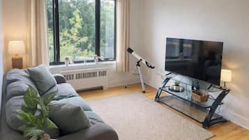Un soggiorno moderno con un divano, una televisione su un mobile, un telescopio e una finestra che si affaccia su alberi.