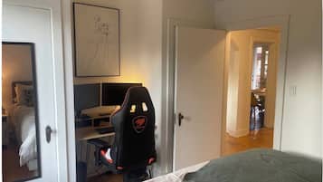 Una camera da letto con un letto, una scrivania con un computer, una sedia e una porta che dà su un'altra stanza.